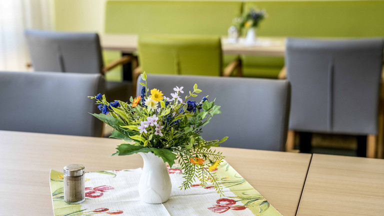 Ein Tisch mit Tischdecke und Stühlen und Blumenschmuck in den Räumen der Wohnpflege-Einrichtung des Albertinen Haus - Albertinen Haus - Wohnpflege-Einrichtung - Hamburg