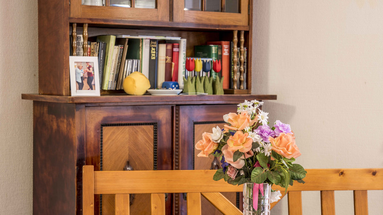 Blumenvase auf Tisch, dahinter Schrank mit Büchern - Max Herz Haus Blumenvase auf Tisch, dahinter Schrank mit Büchern - Max Herz Haus